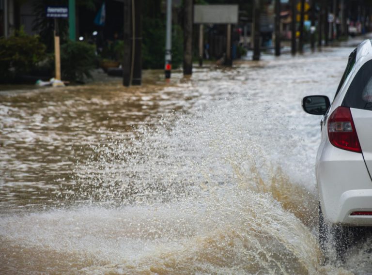 carro-dirigindo-em-estrada-inundada-com-fluxo-de-agua-de-inundacao-na-estrada-apos-chuva-forte-e-ondas-de-tempestade