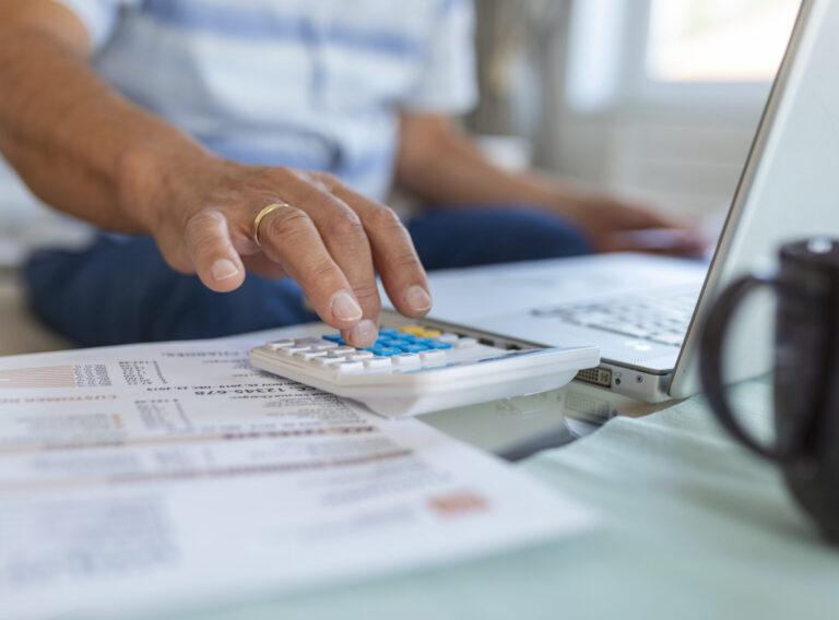 Serious elder senior grey-haired grandpa using calculator counting bank loan payment holding papers at home, focused mature old man doing paperwork calculating bills managing finances sit on sofa Serious elder senior grey-haired grandpa using calculator counting bank loan payment holding papers at home, focused mature old man doing paperwork calculating bills managing finances sit on sofa