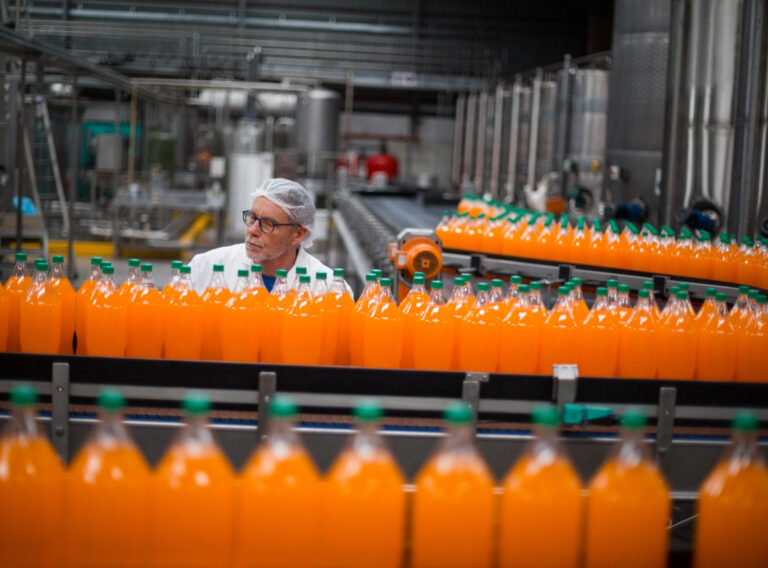 Factory engineer monitoring filled juice bottle on production line in bottle factory